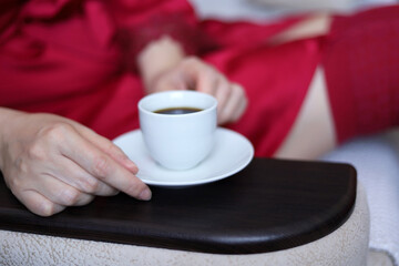 Hand of woman in red knee socks and nightie sitting with coffee cup on a sofa. Relaxation at home, fresh morning