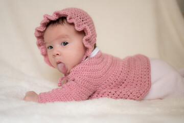 beautiful portrait of adorable mixed ethnicity Asian Caucasian baby girl a few weeks old lying on white blanket wearing a sweet pink hat in new life and newborn concept