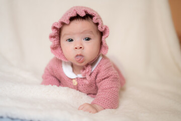 beautiful portrait of adorable mixed ethnicity Asian Caucasian baby girl a few weeks old lying on white blanket wearing a sweet pink hat in new life and newborn concept