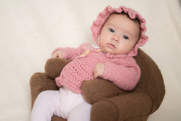 sweet portrait of adorable mixed ethnicity Asian Caucasian baby girl a few weeks old sitting on mini sofa couch wearing a sweet pink hat and jacket