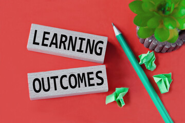 LEARNING OUTCOMES - words on wooden bars on a red background with a handle, cactus and papers