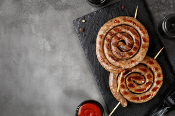 Grilled pork sausages with sauce on black stone board on dark background. BBQ. Homemade Snail round sausage.