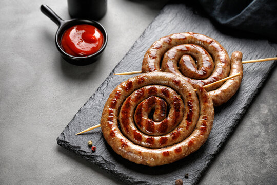 Grilled pork sausages with sauce on black stone board on dark background. BBQ. Homemade Snail round sausage.