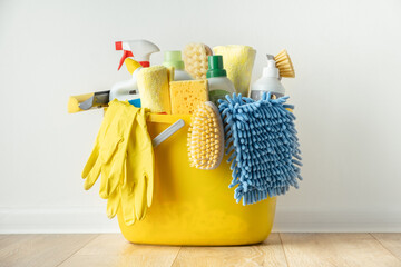 Brushes, bottles with cleaning liquids, sponges, rag and yellow rubber gloves on white background. Cleaning supplies in the yellow bucket on the wooden floor. Cleaning company service advertisement