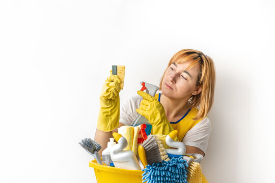 Happy young caucasian woman in a uniform wearing yellow rubber gloves and holding bucket full of cleaning supplies. Cleaning company service advertisement. Free space for text. House cleaning concept