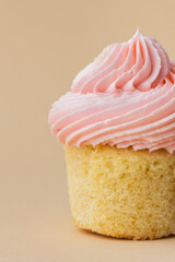Close-up of vanilla cupcake with pink whipped butter cream top. Cream cheese frosting on muffin decorated with little pink heart shaped chocolate topping. Beige background. Happy Valentine's Day