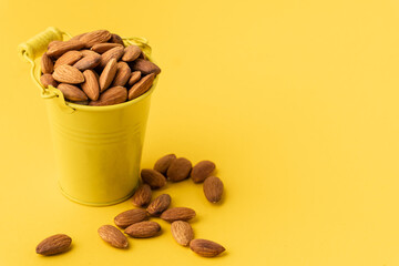 Dried almonds in a yellow bucket on the yellow background. Nuts stacked together randomly with a...
