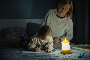 Mother and little daughter studying and drawing in a complete darkness during electricity outage....
