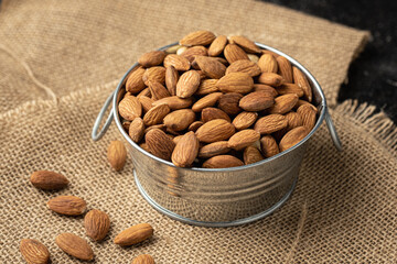 Metal bowl full of almonds on a sackcloth. Pile of nuts stacked together randomly on the burlap background. Healthy nutrition concept