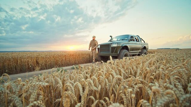 Close up soldier getting out of the car near in a wheat field, dressed in camouflage. Blue sky on sunset. Brave man. War. Military concept. Slow motion