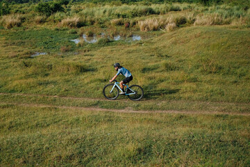 Naklejka premium A young bearded cyclist is biking through a field