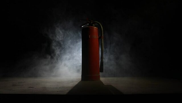 Fire protection concept. Old fire extinguisher on dark foggy background with light. Selective focus