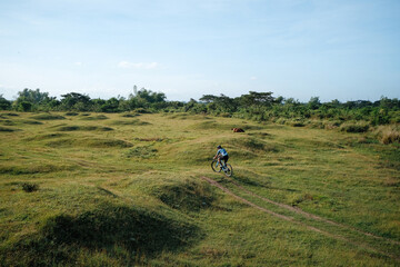 A young bearded cyclist is biking through a field