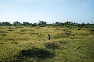 Foto op Plexiglas A young bearded cyclist is biking through a field © Jonathan De Guzman