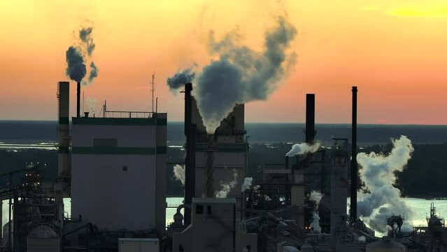 Aerial view of wood processing factory with smoke from production process polluting atmosphere at plant manufacturing yard. Industrial site at sunset