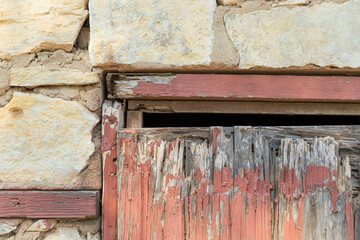 Close up of wood red antique door in bad condition with some rocks in the bottom to prevent animals entering  the structure.