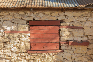 Vintage construction boarded wood red window, in brown stone construction.