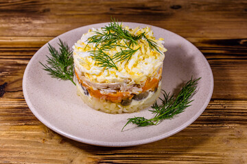 Salad with chicken breast, marinated mushrooms, carrot, eggs, boiled potato and mayonnaise on a wooden table