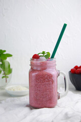 raspberry coconut smoothie with ice in a jar with straw, white background 