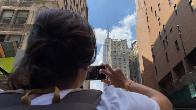 young woman from behind taking photos with mobile phone new york skyscrapers iconic buildings manhatan travel adventure summer lifestyle tourism