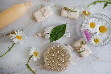 Massage brush, soap, chamomile flower on a light background