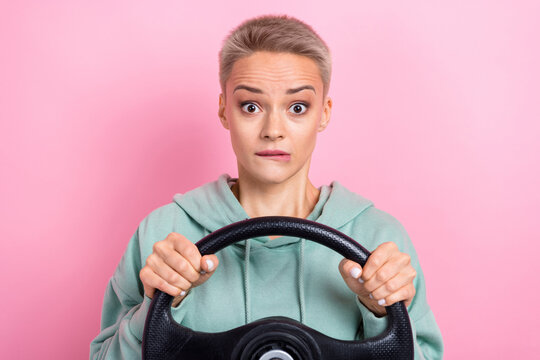 Photo portrait of pretty young girl nervous bite lips hold steering wheel dressed stylish khaki clothes isolated on pink color background