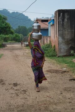 A woman walks with a pitcher of water on her head in a small village near Panna National Park. Madhya Pradesh, India