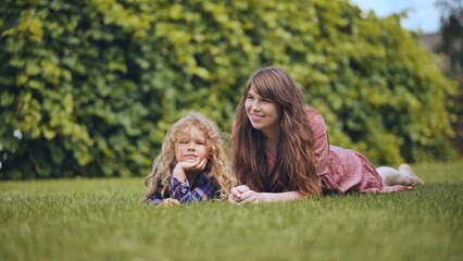 A mother and her daughter lie on the grass in the garden.