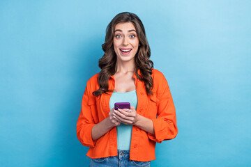 Photo of adorable excited woman dressed orange jacket reading message modern gadget isolated blue color background
