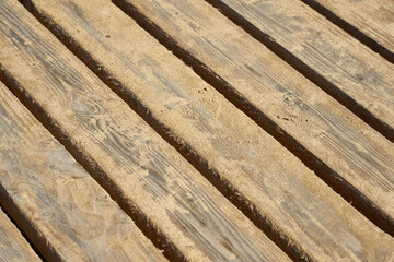 The wooden planks of the old bridge are covered with sand as a background.