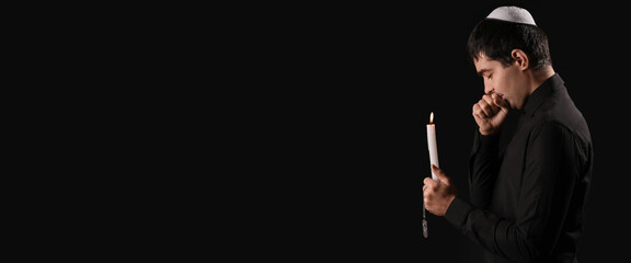 Praying Jewish man with burning candle on dark background with space for text. International...