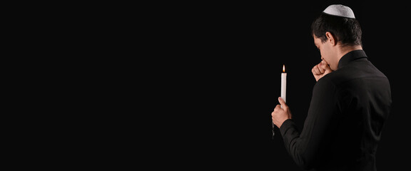 Praying Jewish man with burning candle on dark background with space for text. International Holocaust Remembrance Day