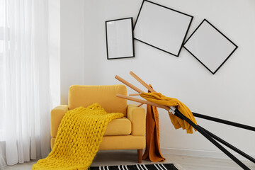 Interior of messy living room with yellow armchair, clothes stand and crooked frames