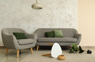 Interior of living room with armchair, sofa and overturned table near light wall