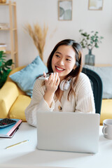 Positive young female in casual clothes smiling and looking at camera while sitting on sofa and working on remote project at home