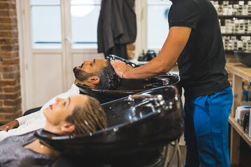 Couple visit at beauty salon. Two people using shampoo chairs in a hairdresser salon. Unrecognizable hairstylist washing hair of two clients. High quality photo