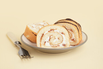 Plate with pieces of sweet sponge cake roll on color background