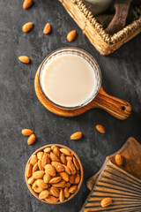 Wooden board with glass of almond milk and nuts on dark background