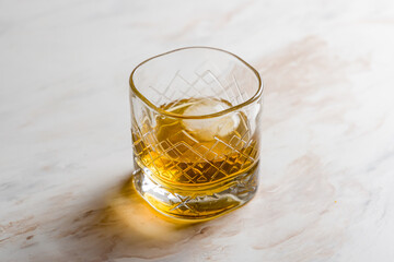 a glass of whiskey and round ice on white marble table