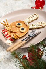 Plate with bunny made of pancakes, fruits and Christmas decor on grunge table, closeup