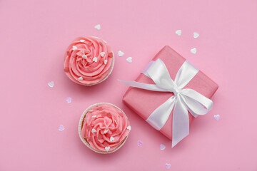 Tasty cupcakes, hearts and gift for Valentine's Day on pink background
