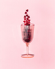 Red hearts in glass on pastel light pink background. Minimalistic love concept. Creative Valentine's Day flat lay idea.