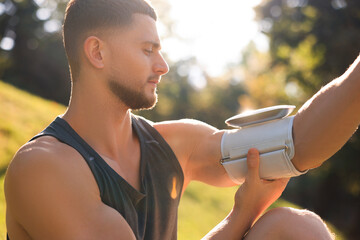 Attractive serious man checking blood pressure with modern monitor after training in park