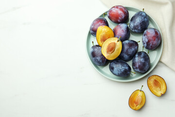 Tasty ripe plums on white table, flat lay. Space for text