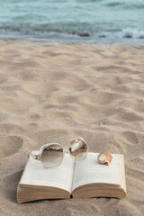 Beautiful sunglasses, book and shell on sand near sea, space for text
