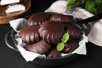 Delicious chocolate covered marshmallows with mint on black table