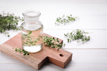 Obraz na płótnie Canvas Bottle of thyme essential oil and fresh plant on white wooden table, space for text