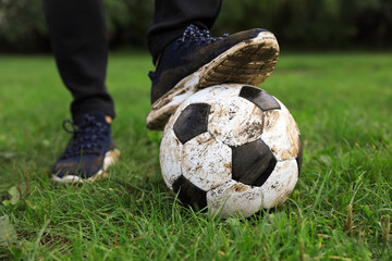 Man with dirty soccer ball on green grass outdoors, closeup