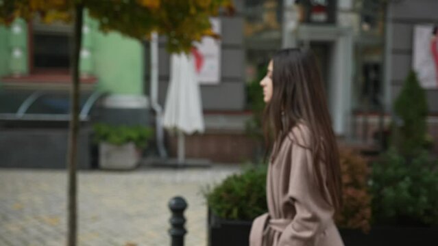 Young woman in an autumn coat walks down the street