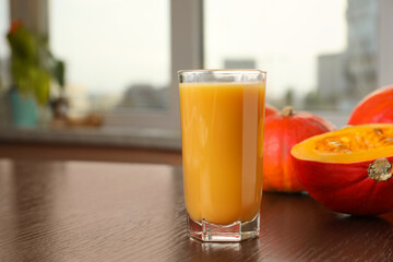 Tasty pumpkin juice in glass on wooden table indoors. Space for text
